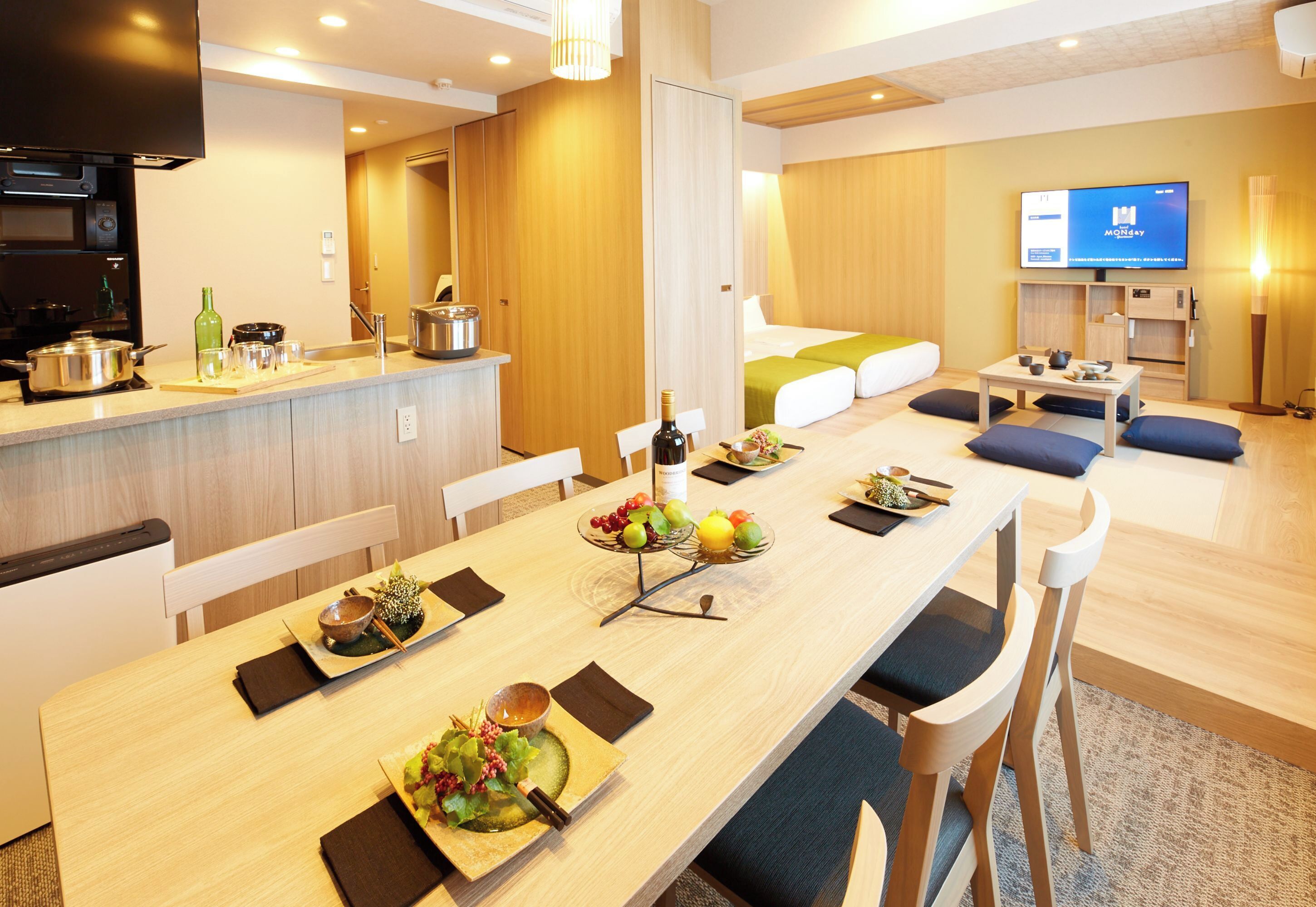 A modern hotel room with a dining area, kitchenette, and a TV.