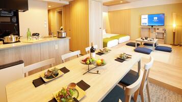 A modern hotel room with a dining area, kitchenette, and a TV.