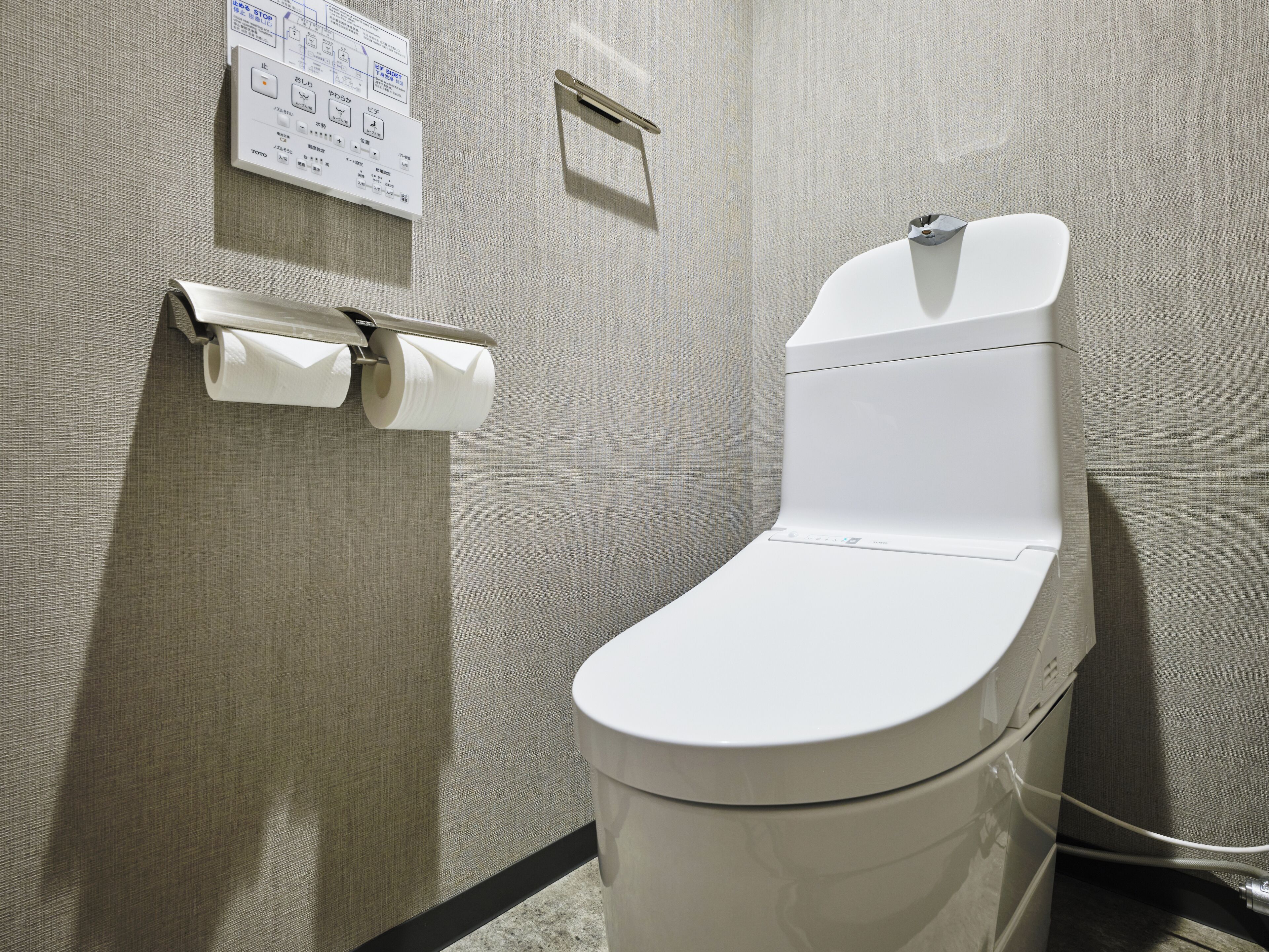 Des toilettes modernes dotées d’un panneau de commande, d’un porte-rouleau de papier toilette et d’un petit panneau affiché sur le mur.