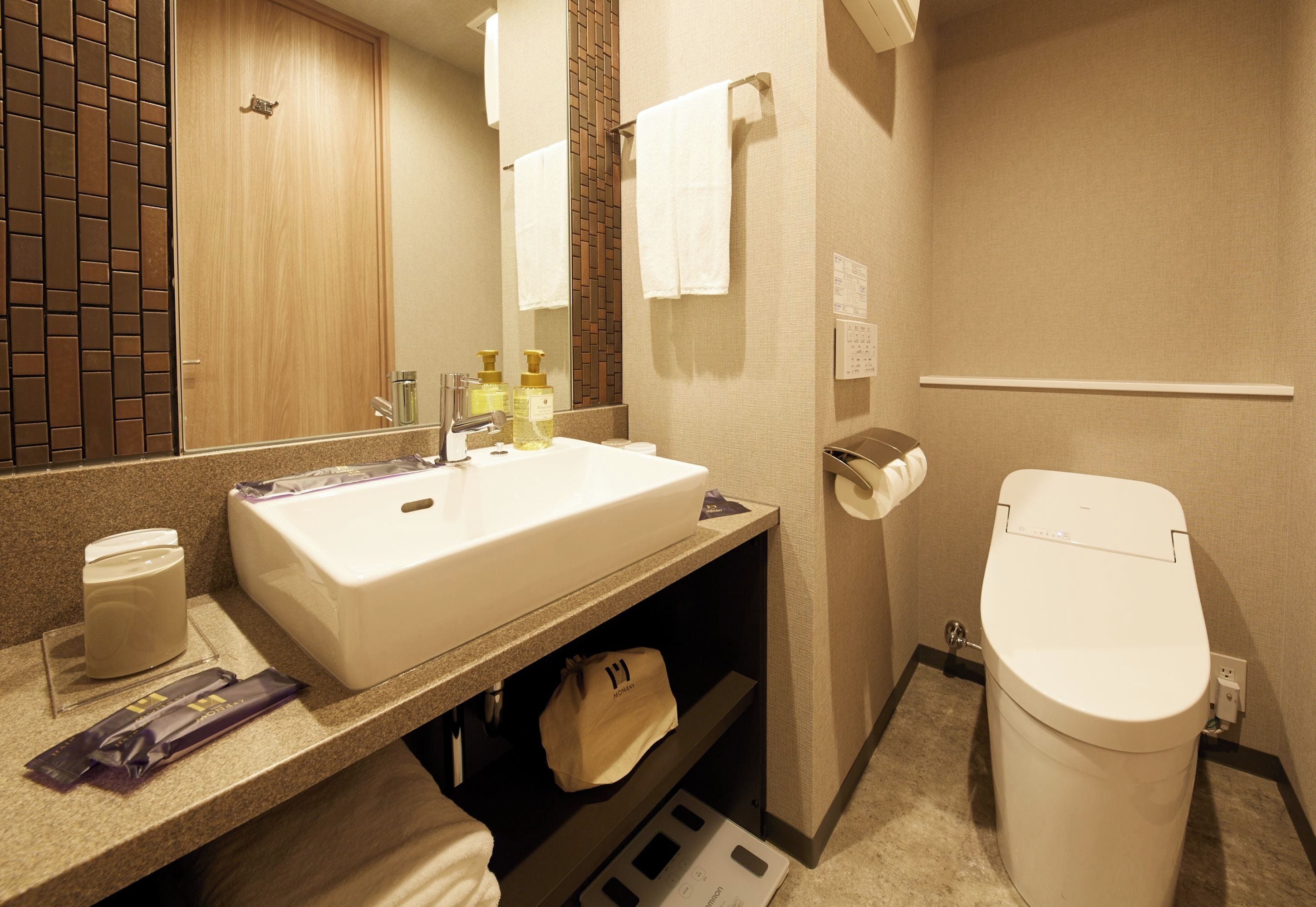 Et badeværelse på et hotel med håndvask, spejl, toilet og håndklædestang.