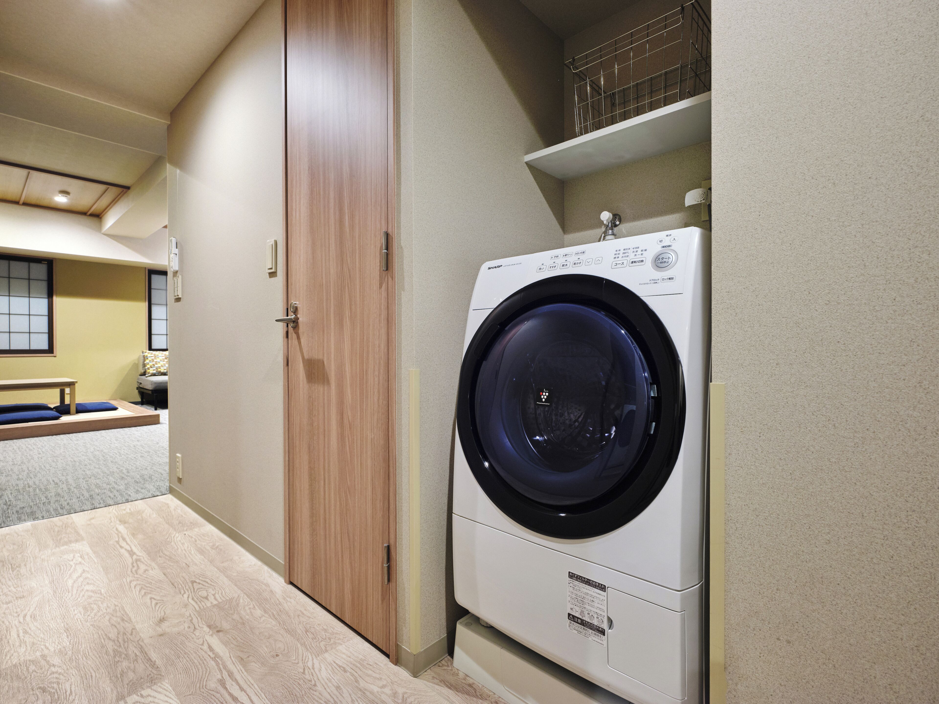 A laundry room with a front-loading washing machine, a wooden door, and a bench with cushions.