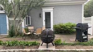 A backyard with a grill, a table with chairs, a small tree, and a white door. - West Harwich- Cozy Cape House walking distance to Dennis Port & Bell's Neck path (Harwich)