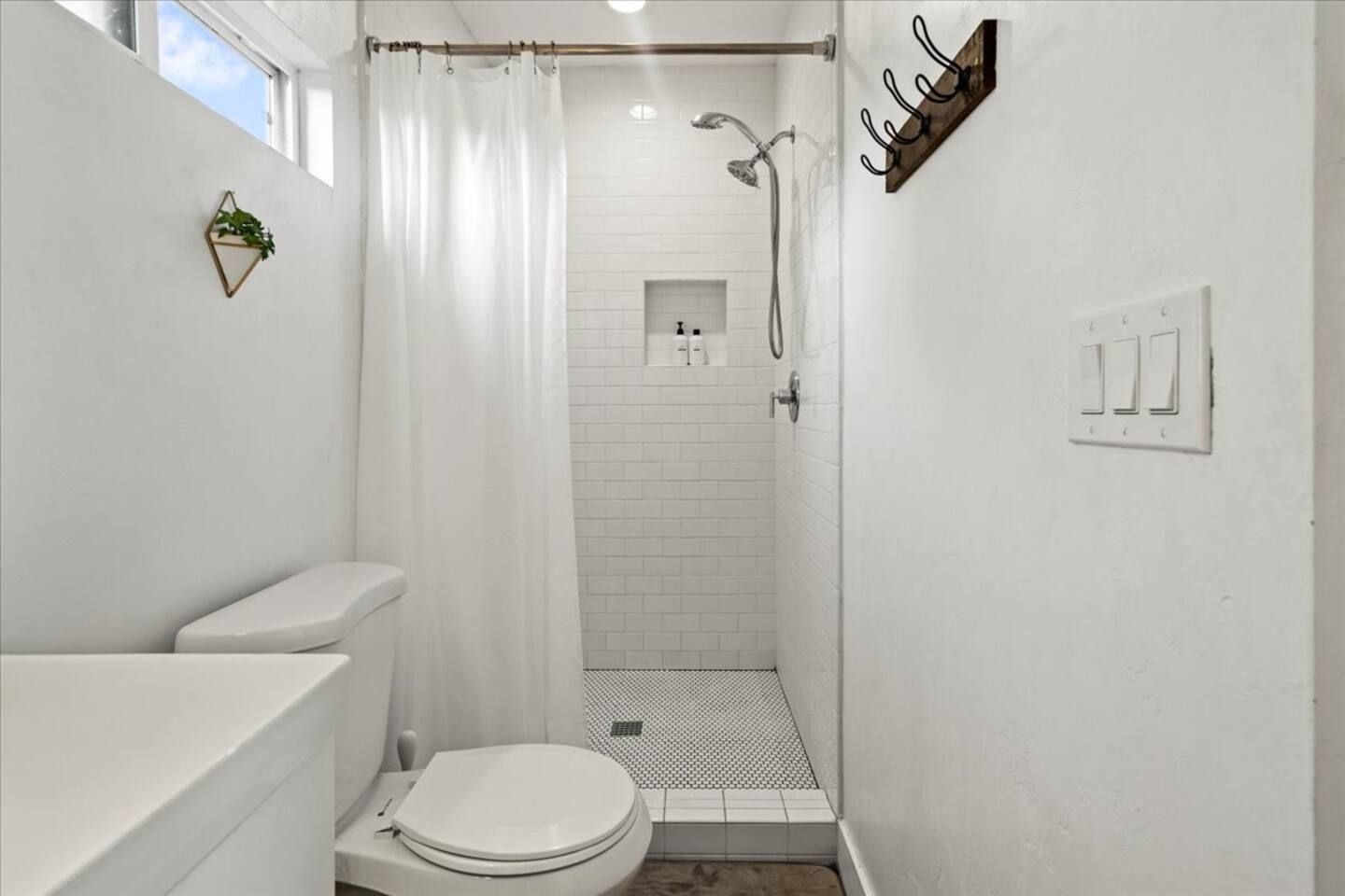 Une petite salle de bain blanche, équipée d’une douche, de toilettes et d’un porte-serviettes.