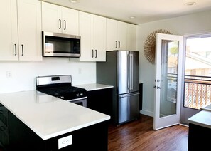 A modern kitchen with white cabinets, a stainless steel microwave, a refrigerator, and a gas stove. - Beautiful BOHO Home by Beach, Downtown + Shops (San Diego)