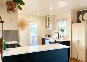 A modern kitchen with a central island, white cabinetry, and a view to the outside. - Beautiful BOHO Home by Beach, Downtown + Shops (San Diego)