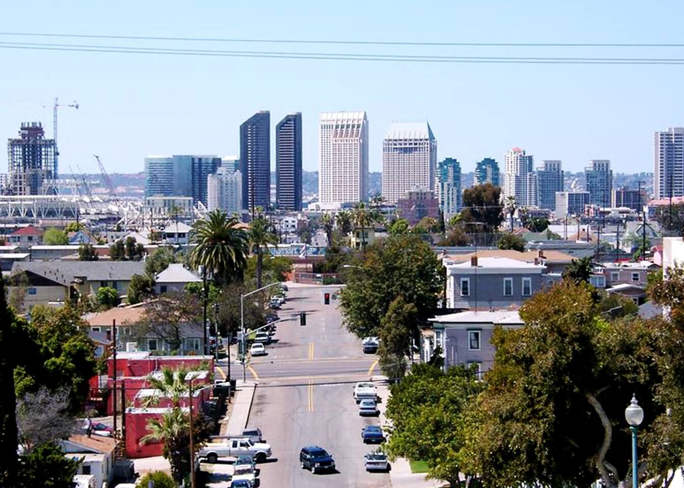 A cityscape with a wide street lined with cars, buildings, and palm trees.