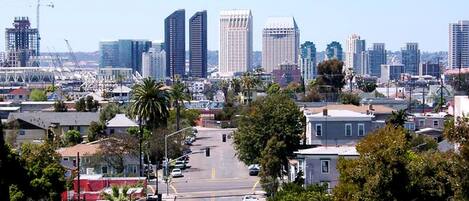 A cityscape with a wide street lined with cars, buildings, and palm trees.