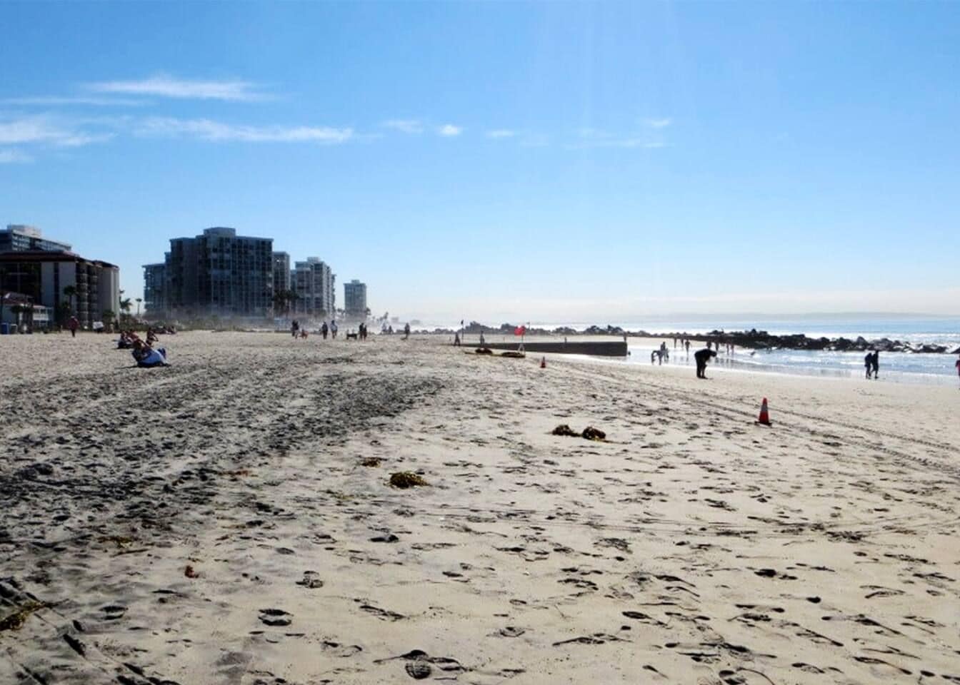 Ein Strand mit Fußabdrücken, einem Steg und Gebäuden im Hintergrund.