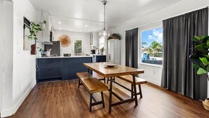 Une cuisine moderne avec une table et un banc en bois, un luminaire suspendu et une vue sur l’extérieur grâce à de grandes fenêtres.