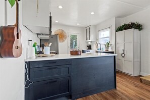 A modern kitchen with a central island, dark cabinetry, and a hanging guitar. - Beautiful BOHO Home by Beach, Downtown + Shops (San Diego)