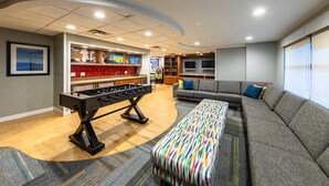 Un salon moderne avec un baby-foot, un canapé et un pouf coloré.