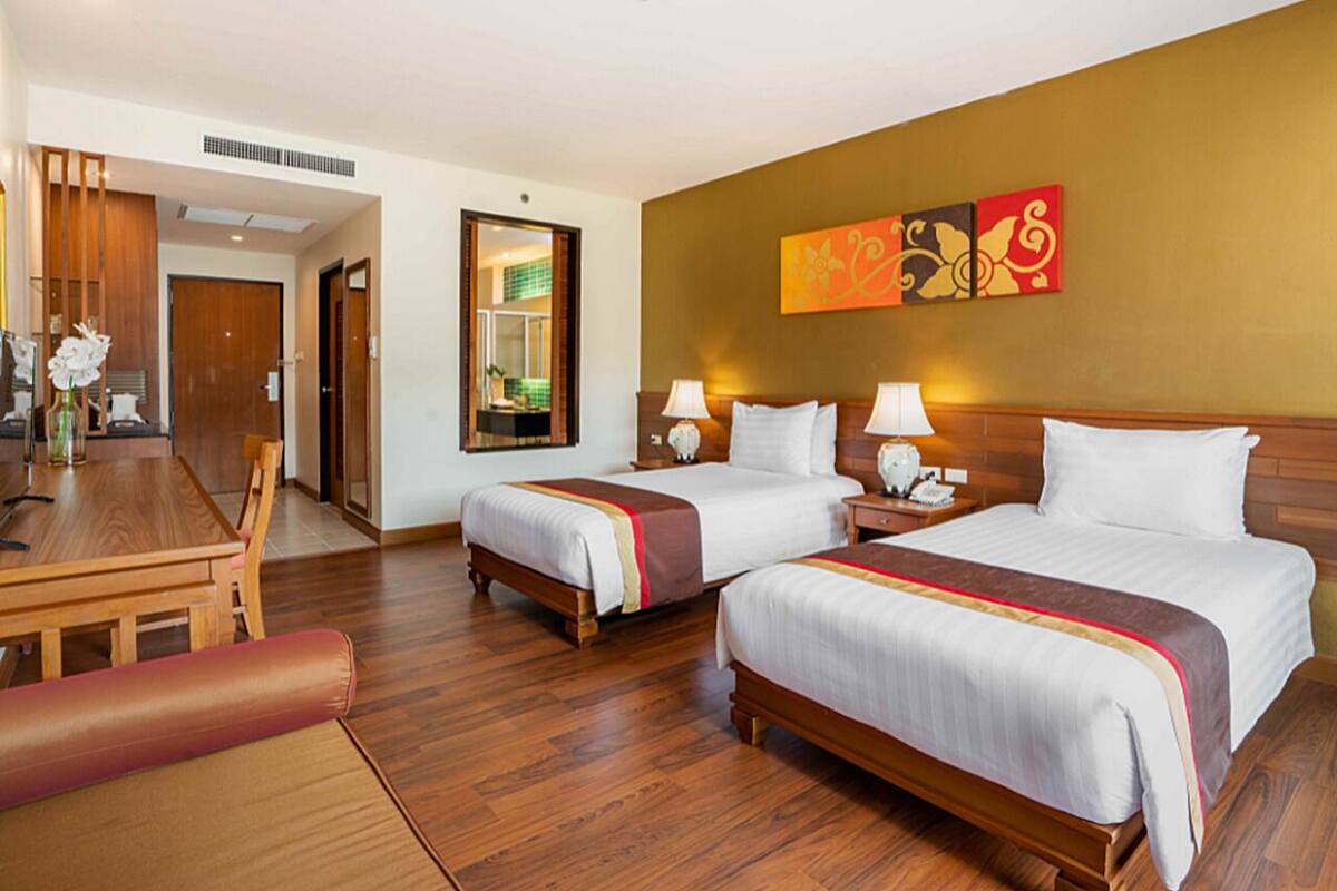 Ein Hotelzimmer mit zwei Betten, einem Holztisch und einem Spiegel.