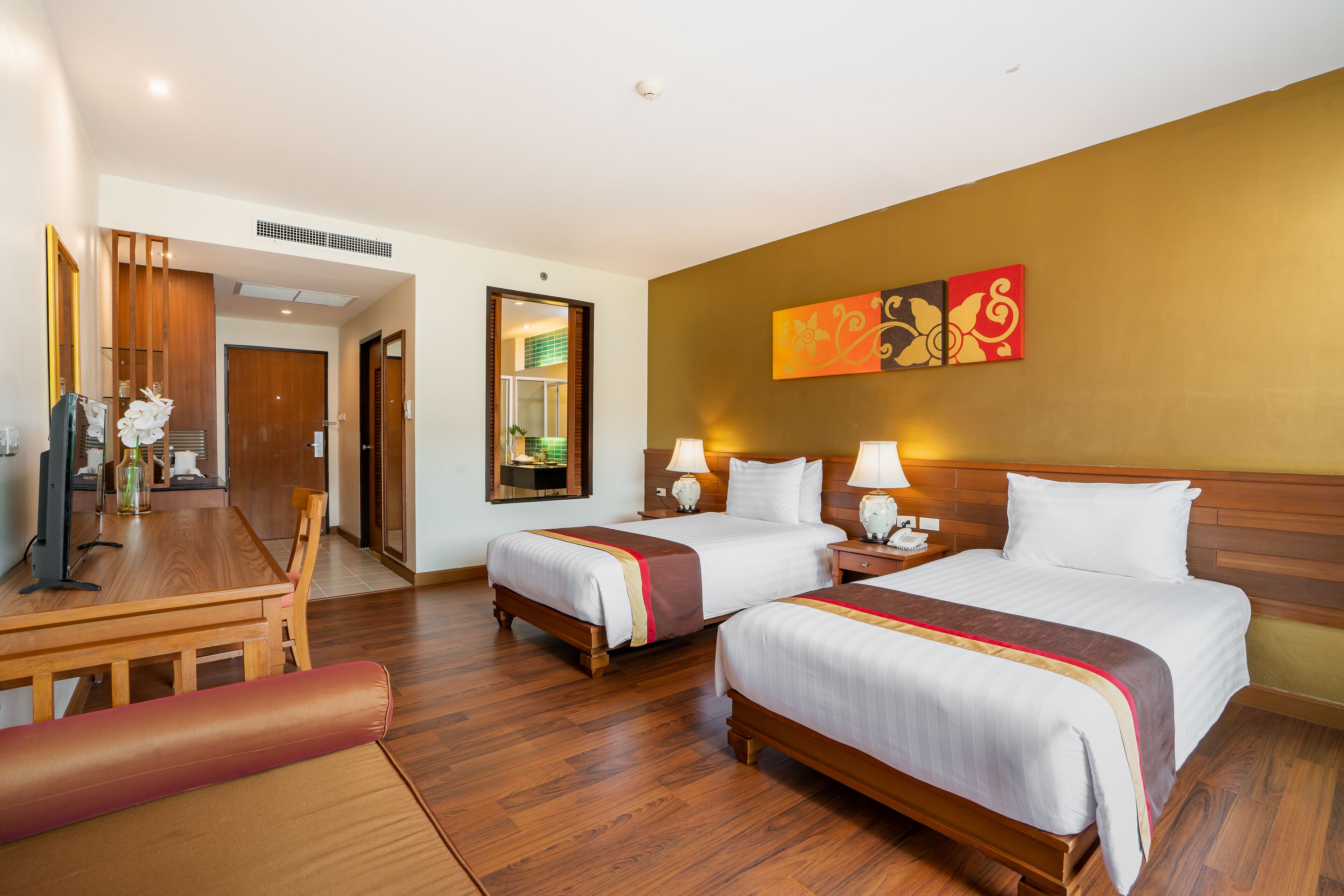 A hotel room with two beds, a wooden desk, and a mirror.