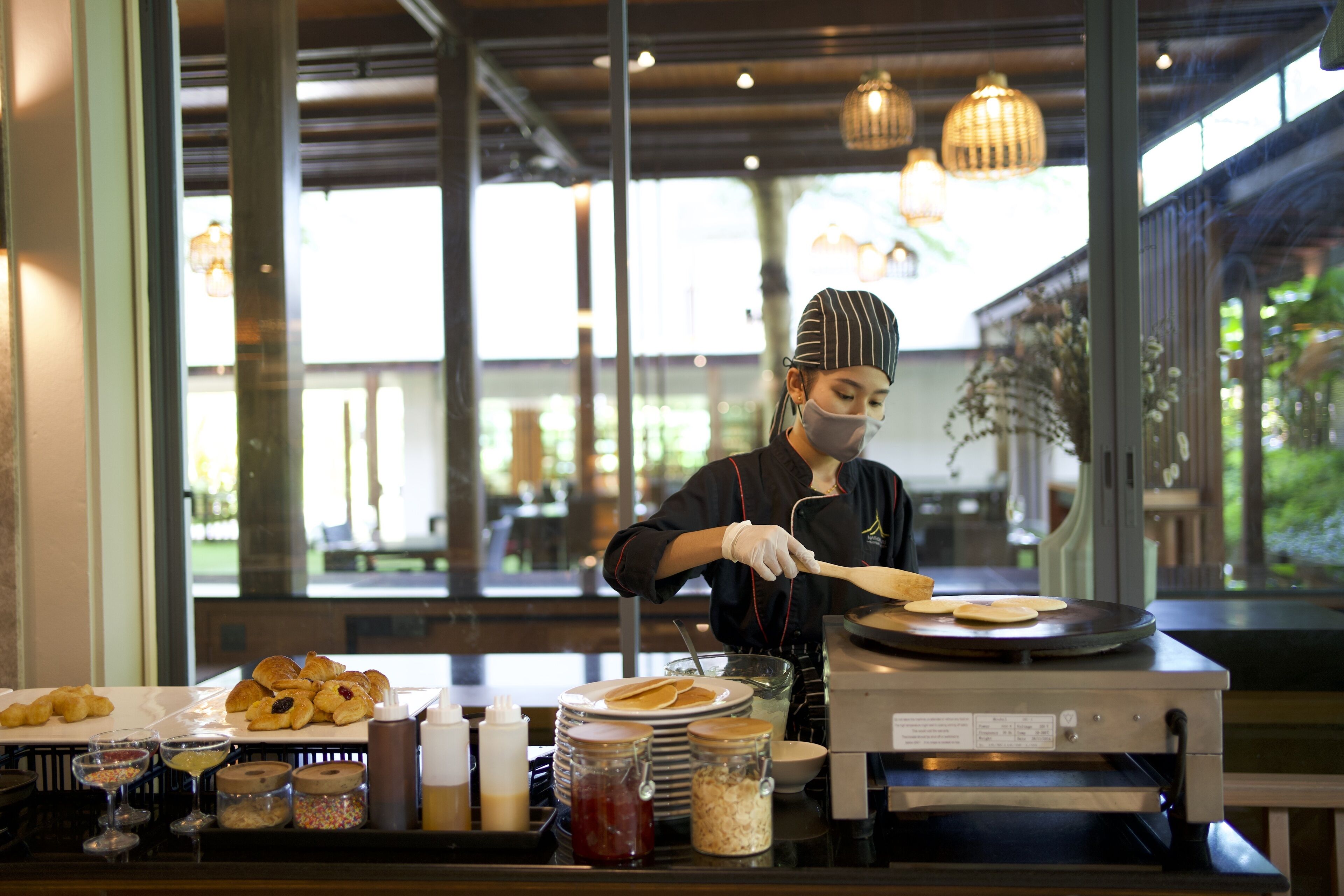 Buffet de café da manhã com pães, acompanhamentos e máquina de panquecas.