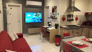 A modern kitchen with a dining area, a TV mounted on the wall, and a red sofa in the living area. - Sea View 2 Bedroom Penthouse Close to Beach Hpi6767 (Marsaskala)