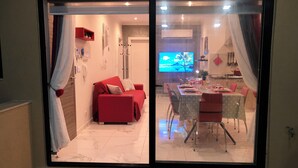 A modern living room with a red sofa, a dining area with a table set for four, and a kitchen visible through a glass door. - Sea View 2 Bedroom Penthouse Close to Beach Hpi6767 (Marsaskala)