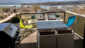 A balcony with a table and chairs, a grill, and potted plants. - Sea View 2 Bedroom Penthouse Close to Beach Hpi6767 (Marsaskala)