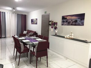 A dining area with a glass table, red chairs, and a white cabinet with decorative items.