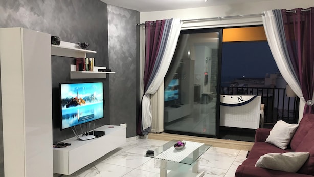Un salon moderne avec un téléviseur à écran plat, un meuble de rangement blanc, une table basse en verre et un canapé rouge.