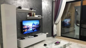 Un salon moderne doté d’un téléviseur à écran plat, d’un meuble de rangement blanc, d’une table basse en verre et d’une porte-fenêtre coulissante donnant sur un balcon.