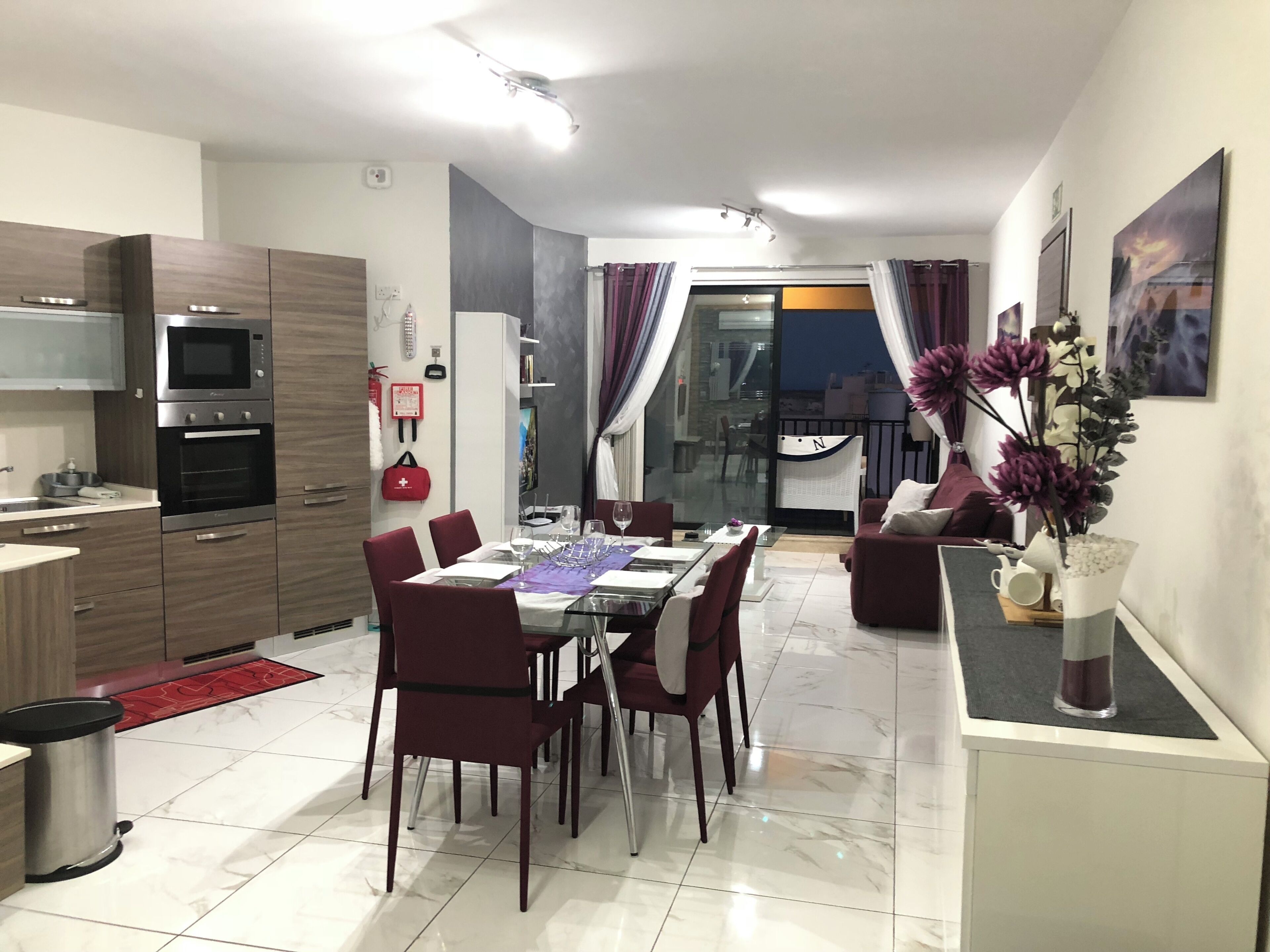 Una cocina moderna con electrodomésticos integrados, un comedor con mesa de vidrio y una sala de estar con sofá y plantas decorativas.