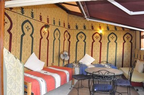 Una habitación con cama, dos sillas, una mesita y un ventilador.