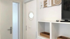 Een kamer met een witte deur, een aan de muur bevestigd horloge en een bord met de tekst 'HELLO'. Er staan twee houten dozen op planken.