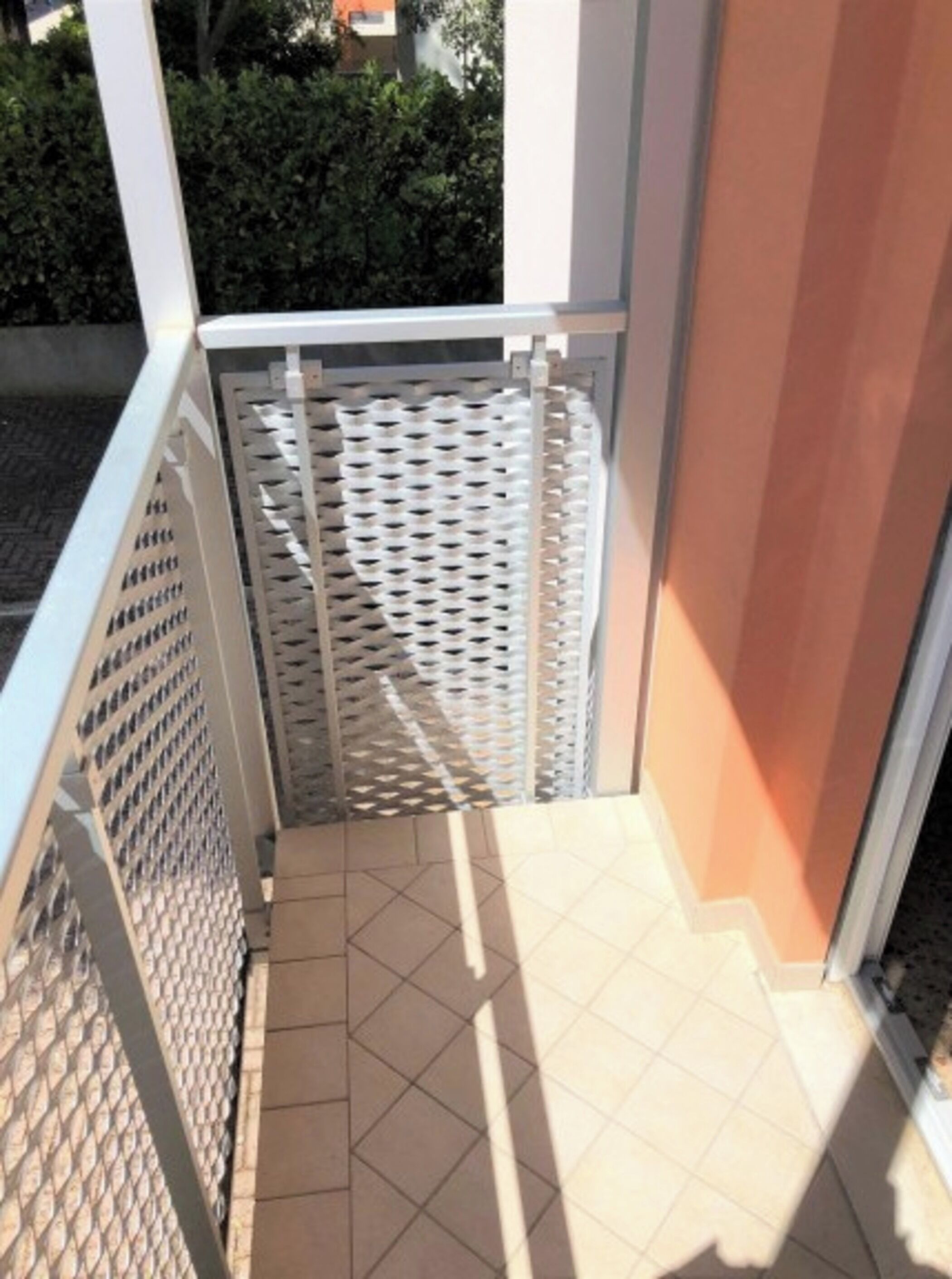 Un coin de pièce avec un sol carrelé, une porte blanche et une barrière en treillis métallique.