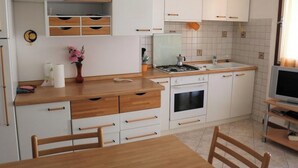 A compact kitchen with white cabinets, a wooden countertop, a stove, and a sink.