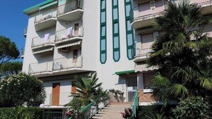 A multi-story building with balconies, a staircase, and surrounding greenery.