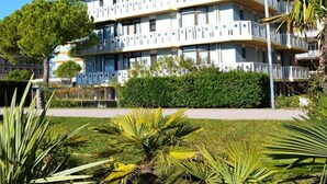 Un edificio de varios pisos con balcones, rodeado de vegetación y un cielo despejado.