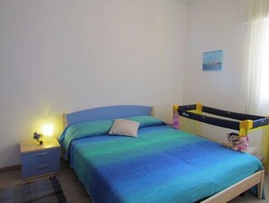 Un dormitorio con cama, mesita de noche, lámpara, ventana con cortinas y estante fijado a la pared.
