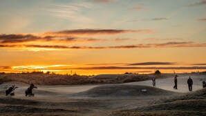 Un campo de golf al atardecer con dunas de arena y golfistas.