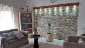 Ein Wohnzimmer mit Steinwand, einem Glastisch, einer Couch und einem Beistelltisch mit einer Vase.