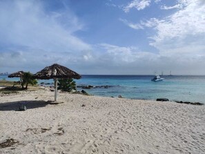 A beach with a thatched umbrella, calm sea, and a boat in the distance. - Rest, Work and fun in the Caribbean (Oranjestad)