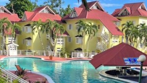 Un complexe hôtelier doté d’une piscine, de bâtiments jaunes aux toits rouges et de palmiers.