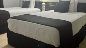 Une chambre d’hôtel avec deux lits, un luminaire rond au plafond et deux œuvres d’art encadrées accrochées au mur.