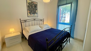 Une chambre à coucher avec un lit, une table de chevet avec une lampe, une fenêtre avec des rideaux et un tableau accroché au mur.