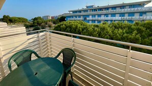 Un balcon avec une table et des chaises, donnant sur un immeuble doté de nombreuses fenêtres et d’une façade bleue.