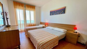 Una camera d'albergo con due letti, una cassettiera in legno, un comodino con una lampada e un quadro raffigurante un panorama urbano.
