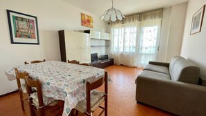 Un soggiorno con tavolo da pranzo, divano e televisione. Sono presenti tende e una luce a soffitto.