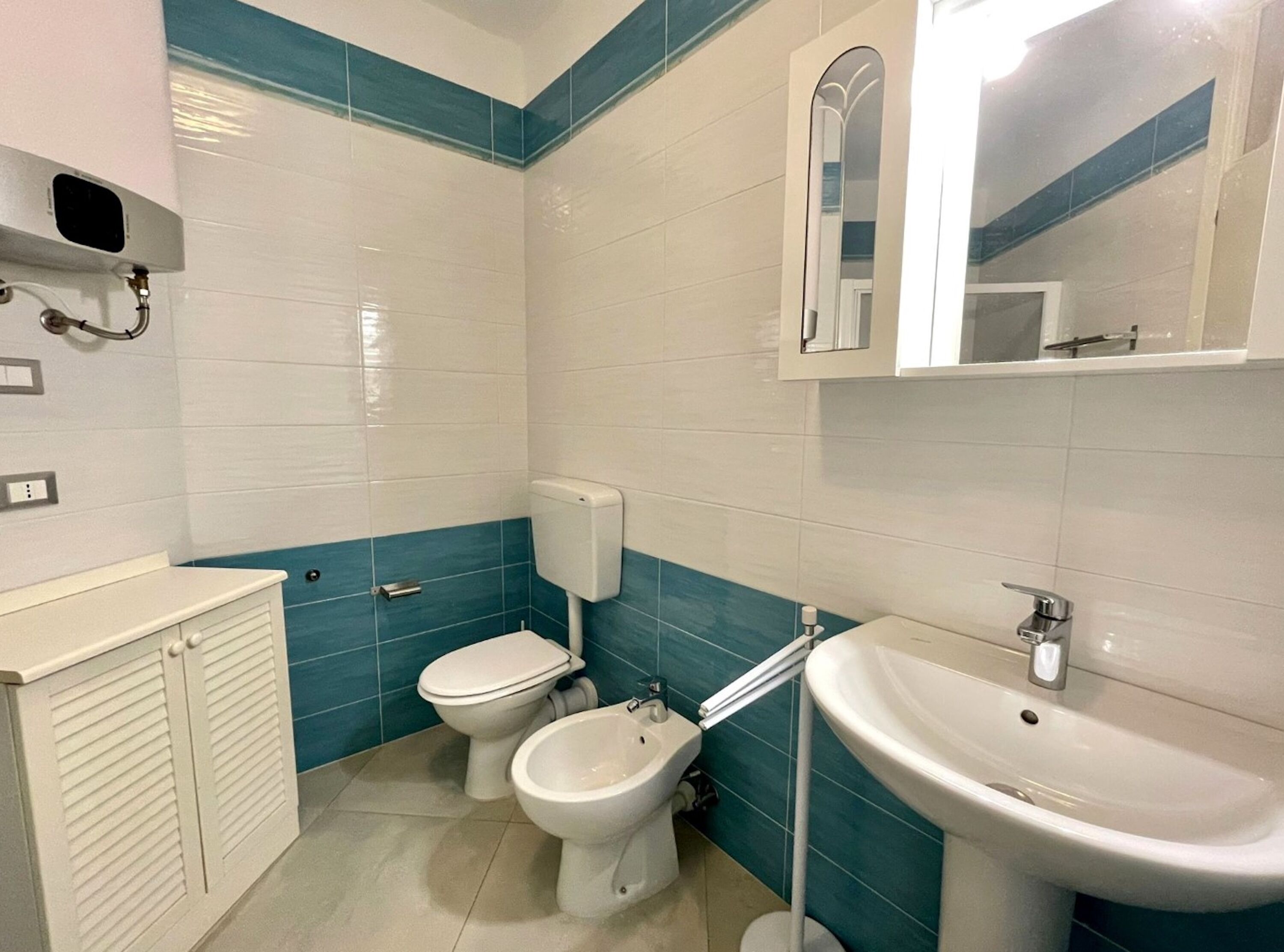 A bathroom with two toilets, a bidet, a sink, and a mirror.