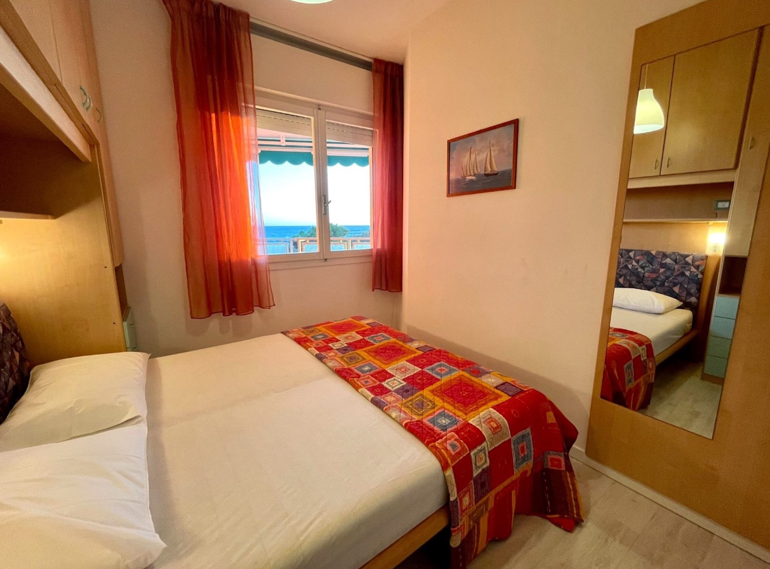 A bedroom with two beds, a window with curtains, a painting, and a mirror.