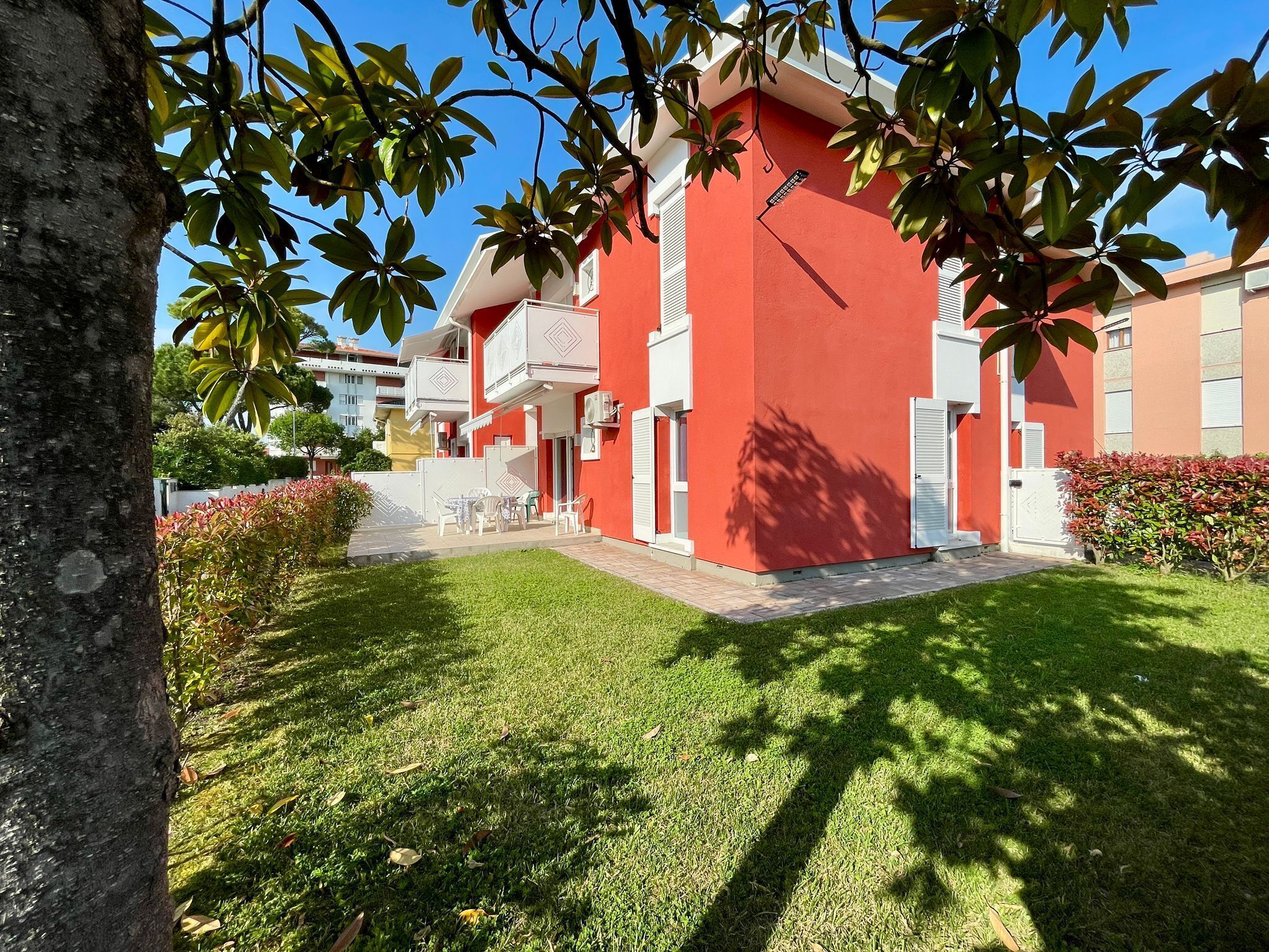 A red building with a balcony, surrounded by a well-maintained lawn and trees.