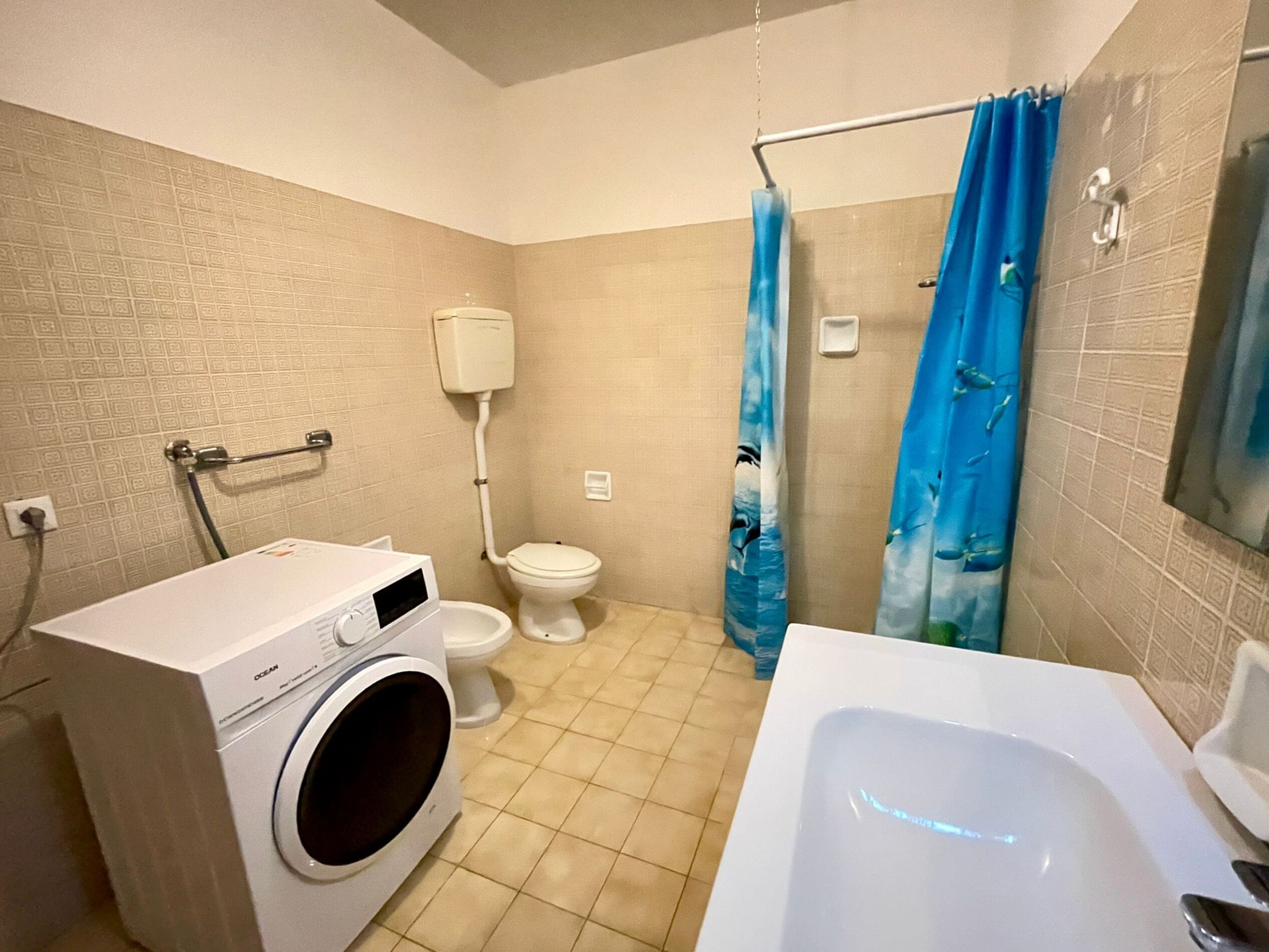 A bathroom with a washing machine, toilet, bathtub, and shower curtain.