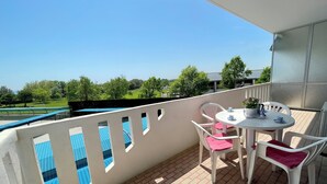 A balcony with a table and chairs, a potted plant, and a view of a green field and trees. - Spacious Apartment Just 200m From the sea (Caorle)