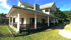 A two-story house with a covered porch and a fenced yard. - Casa Livingston - Luxury Villa - La Digue Seychelles (La Digue)