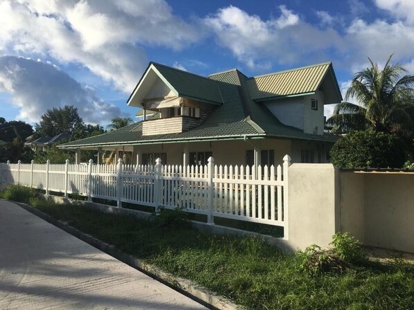 A two-story house with a green roof, white picket fence, and a concrete wall.