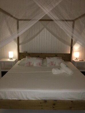 A neatly made bed with white linens and decorative pillows, a wooden headboard, and two bedside lamps on white nightstands. - Casa Livingston - Luxury Villa - La Digue Seychelles (La Digue)