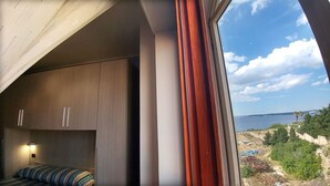 A bedroom with a bed, a wardrobe, and a window with a view of a coastal landscape. - Bluemarine Apartment (Gallipoli)
